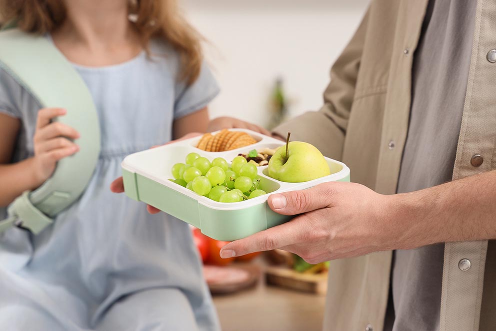 Father preparing a school lunchbox with healthy snacks for his daughter.