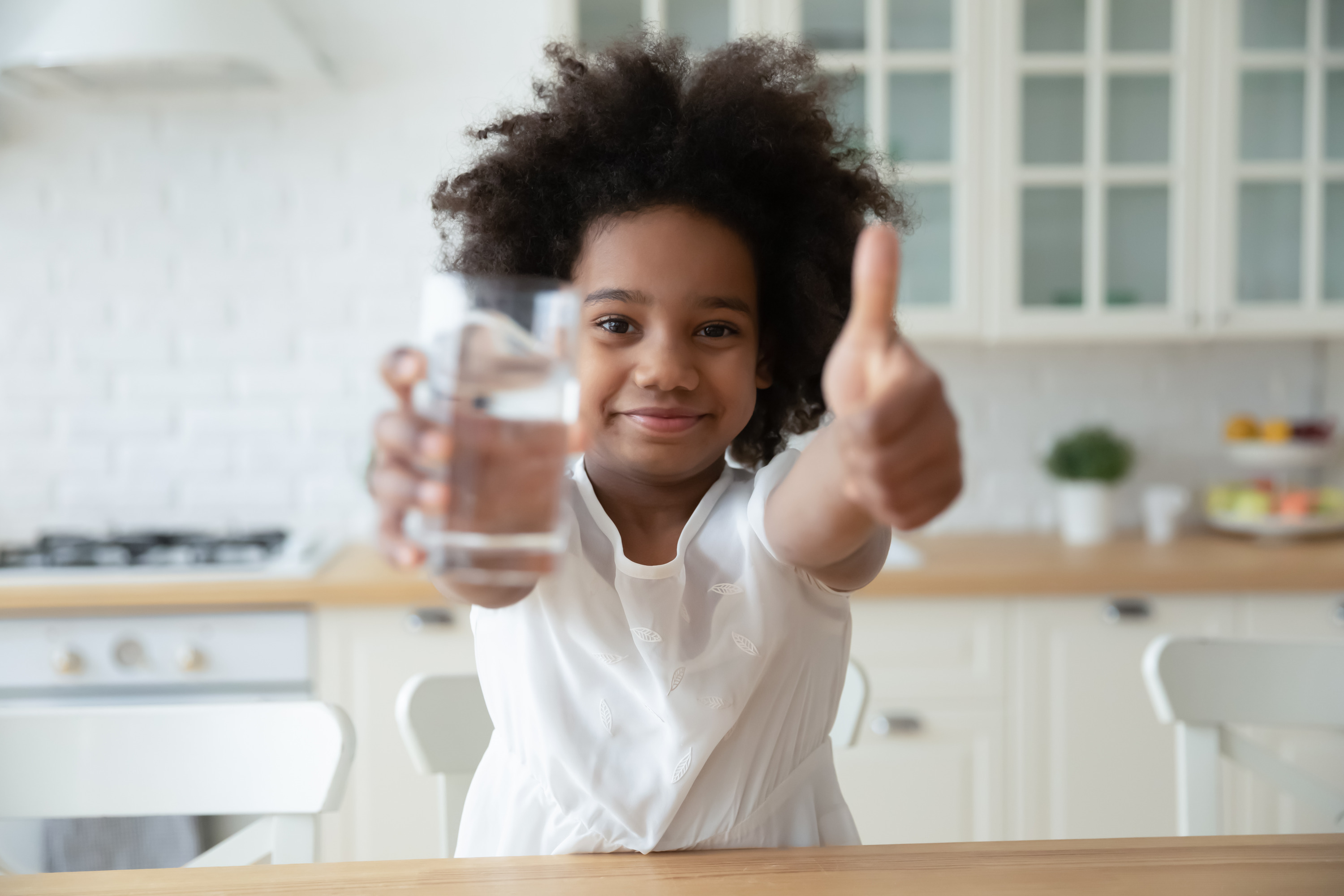 Smiling girl giving a thumbs up while holding a glass of water.
